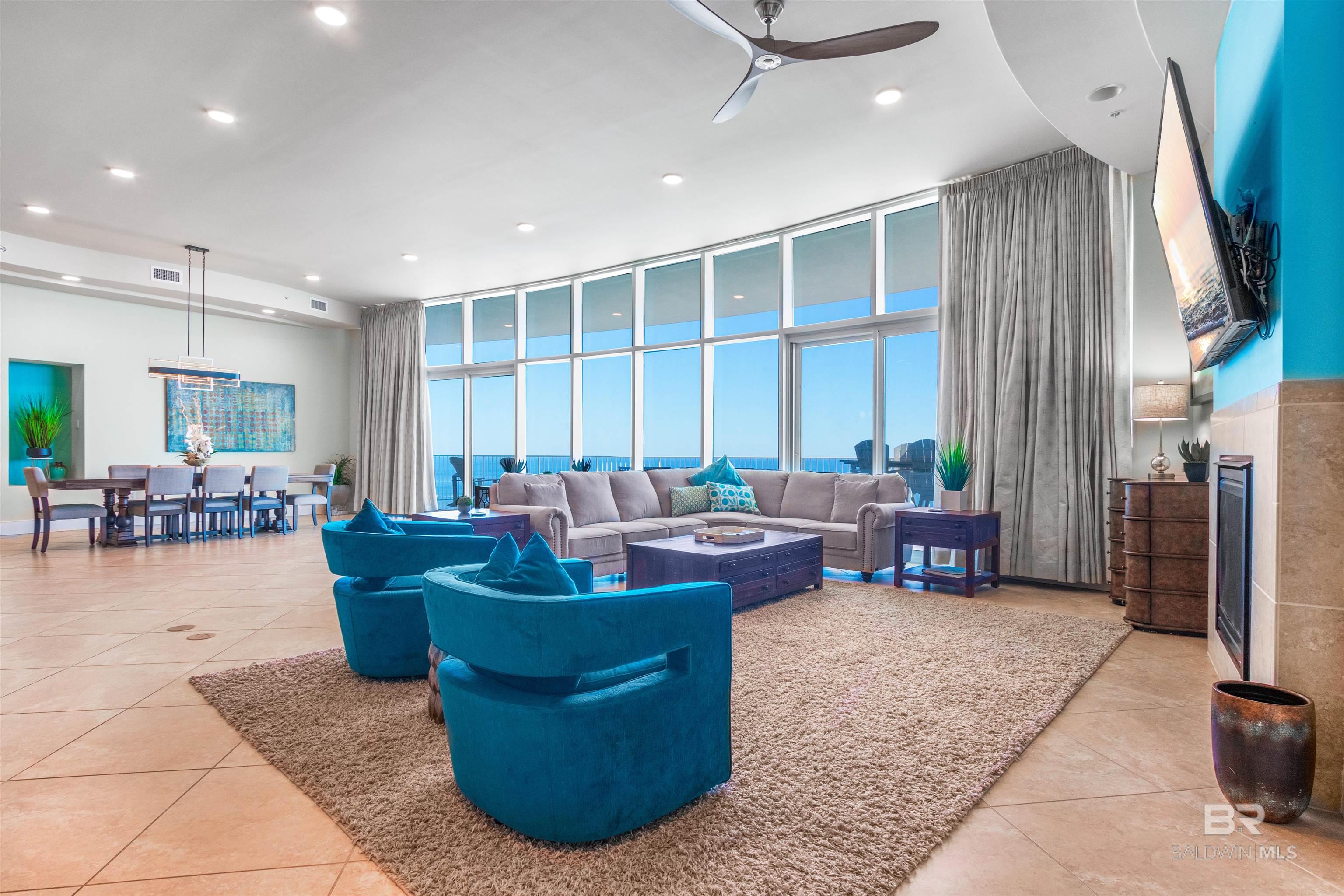 Tiled living room with a towering ceiling, expansive windows, and ceiling fan