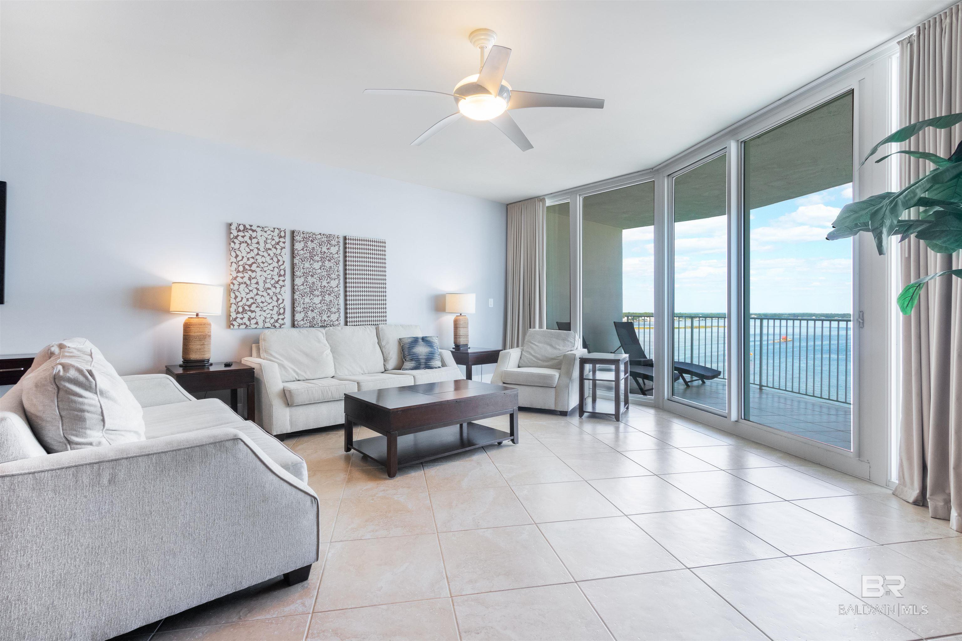 Living room featuring light tile patterned flooring, ceiling fan, a wall of windows, and a water view