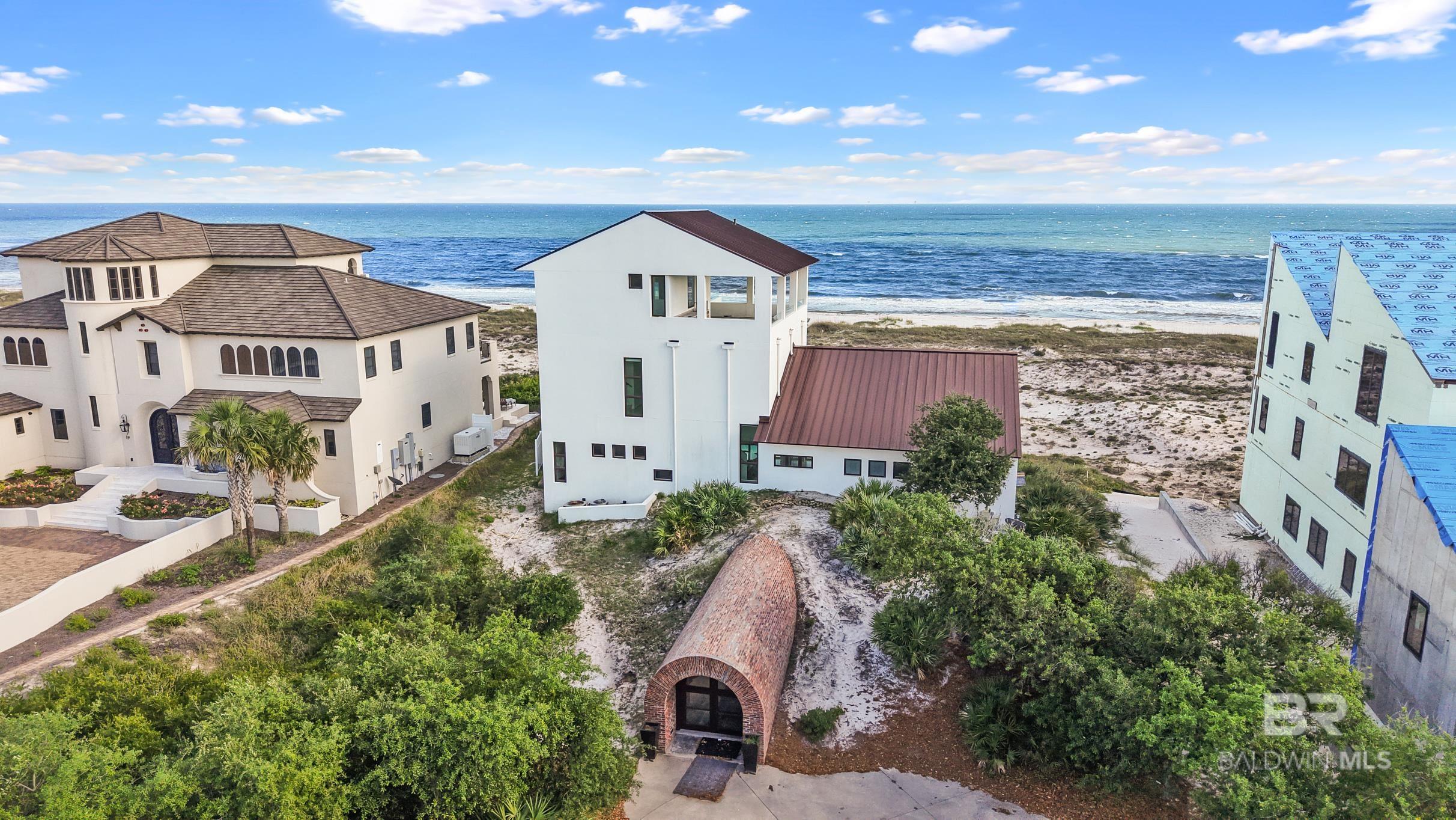 Kiva Dunes Gulf Front Modern Work of Art atop 25 foot dune. The builder, Joe Noah of Noah and Associates, had to move that dune, weighing hundreds of tons, construct an intricate fifty-foot brick tunnel, put the sand dune back over it and re-plant native vegetation. “It’s a modern house with extraordinary features ” Noah says. Summerour designed the residence to be built into the land; unique to that spot. His architecture gives permanence and warmth to the home’s state-of-the-art, modern construction. When you open the tunnel door, you enter a magical arched brick passageway beneath the sand, you ascend a concrete stairway, past two, eight-foot high zinc sliding doors etched with abstract modernist patterns. These doors partition off guest and main living areas and dramatically mark the end of your journey to reach the heart of the home. You are now face to face with an indescribably breathtaking view of the gulf. A 54-foot fresh water lap pool shimmers at your feet on the veranda. Inside the home, scored concrete floors are glazed in a white epoxy finish. The metallic element, zinc, traditionally thought of as a corrosion resistant coating for other metals, becomes a unifying design theme throughout the residence; from the zinc roof shingles to the first floor ventless gas floating fireplace. You move effortlessly among three levels in a restful cocoon of serenity and sensual luxury that includes guest spaces, luxuriously appointed baths, a master suite, recreation space, study/office, third floor porch with wrap-around views, with indoor/outdoor fireplaces. It took more than three years and the combined talents of a world-class architect and his team to mastermind the design and construction of this work of art built to the highest construction standards. You can scour every beachfront property on the Gulf of Mexico and never find any that compare.  Buyer to verify all information during due diligence.