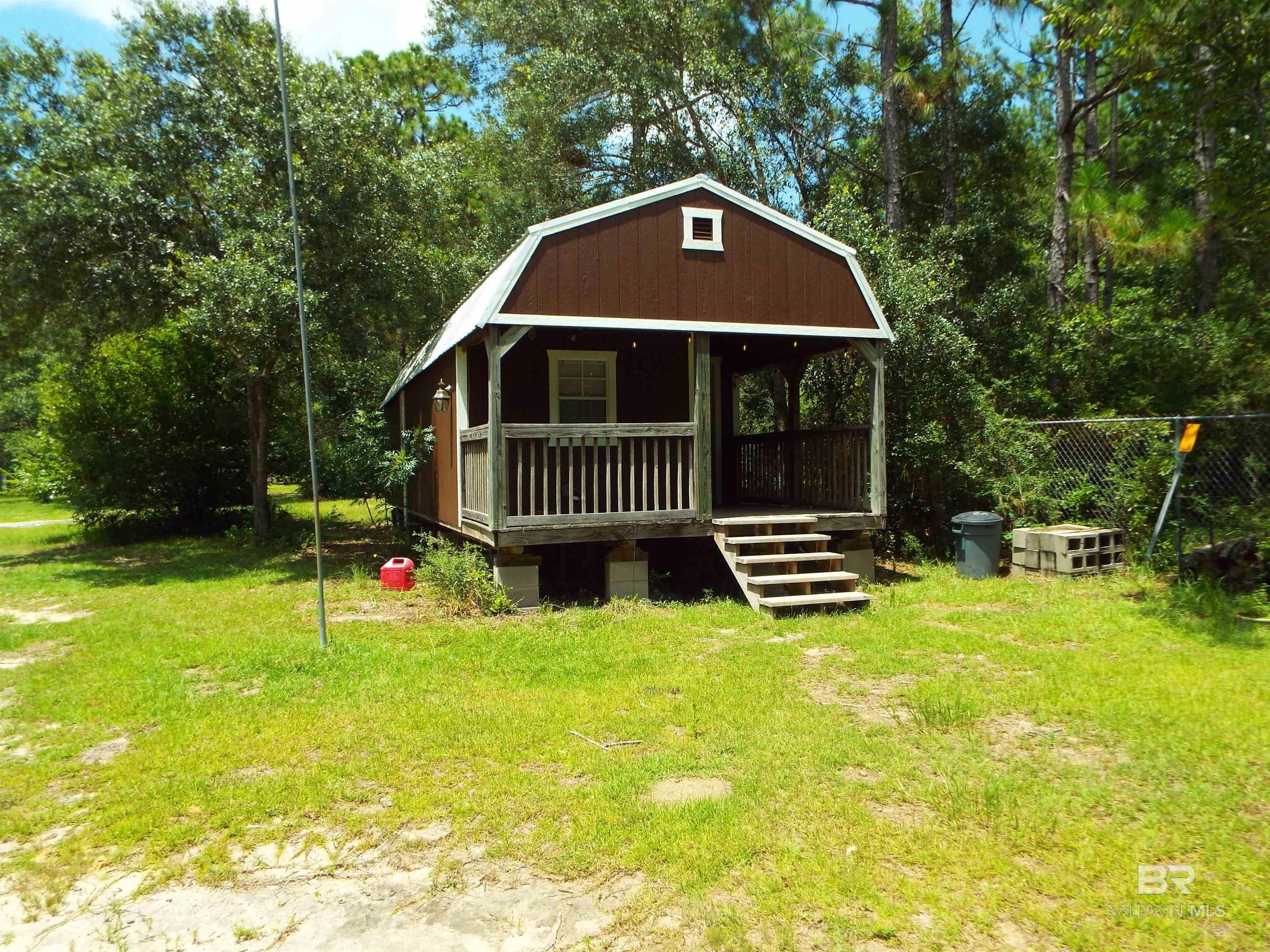 Charming tiny home on 1.19+/- acres! Approx. 14x40 with a covered front porch, this home features a private bedroom, full bath with shower stall, and a cozy living area with lofted storage above. A stacked washer and dryer are conveniently located just across from the bathroom. The kitchen offers butcher block countertops and stainless steel appliances—including barely-used refrigerator, stove, and dishwasher. Floors in the kitchen and bathroom are unfinished, but the seller is leaving tile intended for both areas, as well as extra wood flooring. The home is on permitted septic and well water, providing independence and long-term utility savings. Outside, enjoy a 30x24 carport (approx. 9 ft. tall), a 40x8 storage container in excellent condition, and an insulated shed with A/C. The fenced side yard includes a doghouse, mature trees, and plenty of space to enjoy the outdoors. Power hookup for an RV is also available—ideal for guests or future expansion. The year this home was built is unknown. Sellers think the year was around 2020. This information is deemed reliable, but not guaranteed. Buyer to verify all information during due diligence.