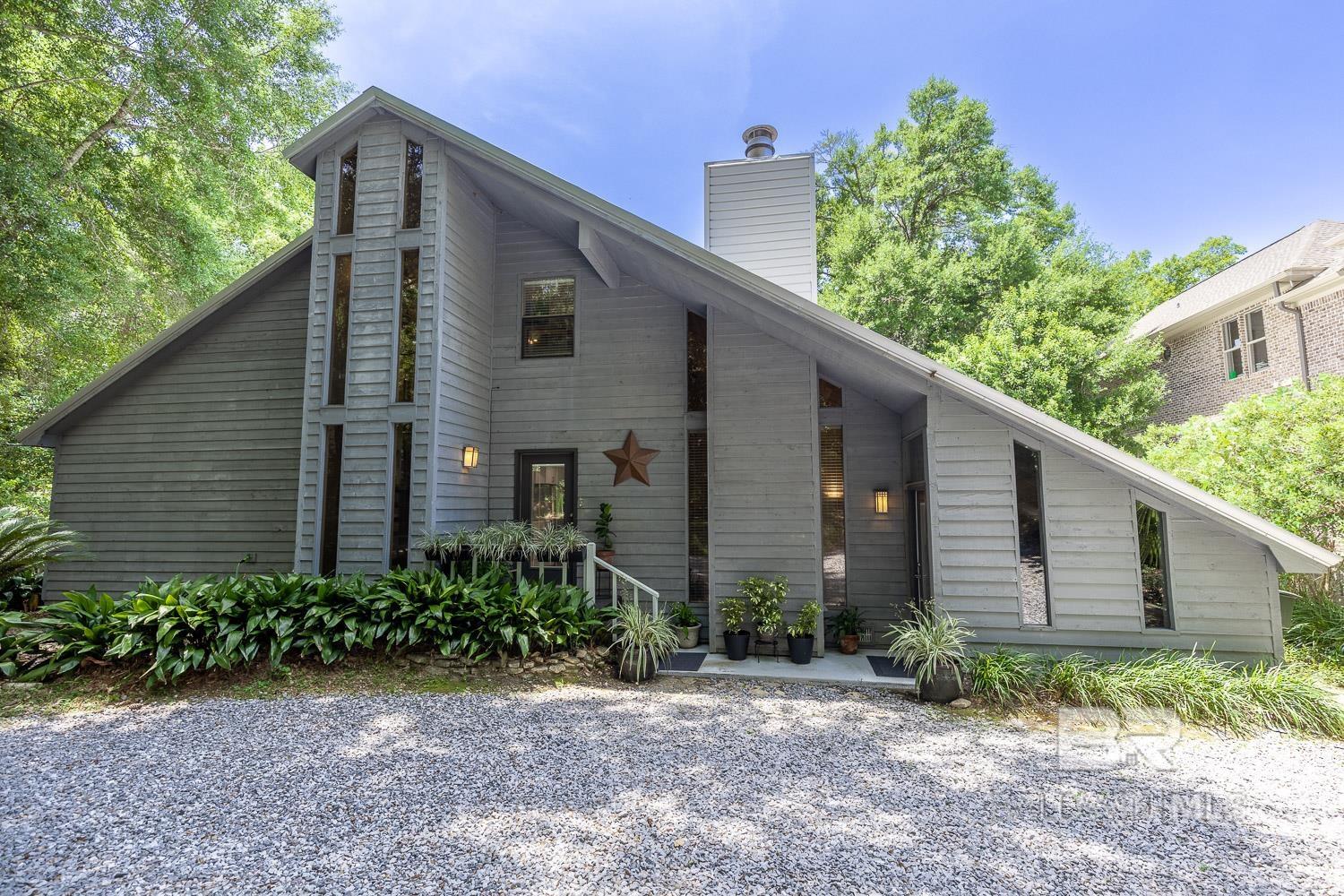 This Old Town Daphne gem is full of soul, sunshine, and stories waiting to unfold! Just one block from May Day Park and the sparkling Mobile Bay, you'll have the pier for fun and fishing, public boat launch, and a playground practically in your front yard but with the privacy of your own lush, fully fenced and maturely landscaped backyard. Inside, this home has charm for days: Contemporary architectural style with cedar siding, main room vaulted wood ceiling with and a wood burning fireplace, warm hardwood floors, a beautifully renovated kitchen space, and a unique bonus feature that all rooms have sliding glass doors out to the deck facing the beautiful backyard. The layout of this home is very flexible with two of the bedrooms on the main level with a full hall bath,  the third bedroom is on the opposite side of the large main room and has a private entrance and full bathroom.  The upstairs could be used as the primary bedroom and has a small separate loft overlooking the living room and the bedroom has lots of space with a full bath, extra dressing area and a private balcony.  The kitchen updates were completed in 2023 and include an induction stove and fabulous Iceberg Quartzite counter tops.  The metal roof, hot water heater and HVAC were replaced just a few years ago. So many different possibilities and a home that you need to see inside to appreciate. Buyer to verify all information during due diligence.