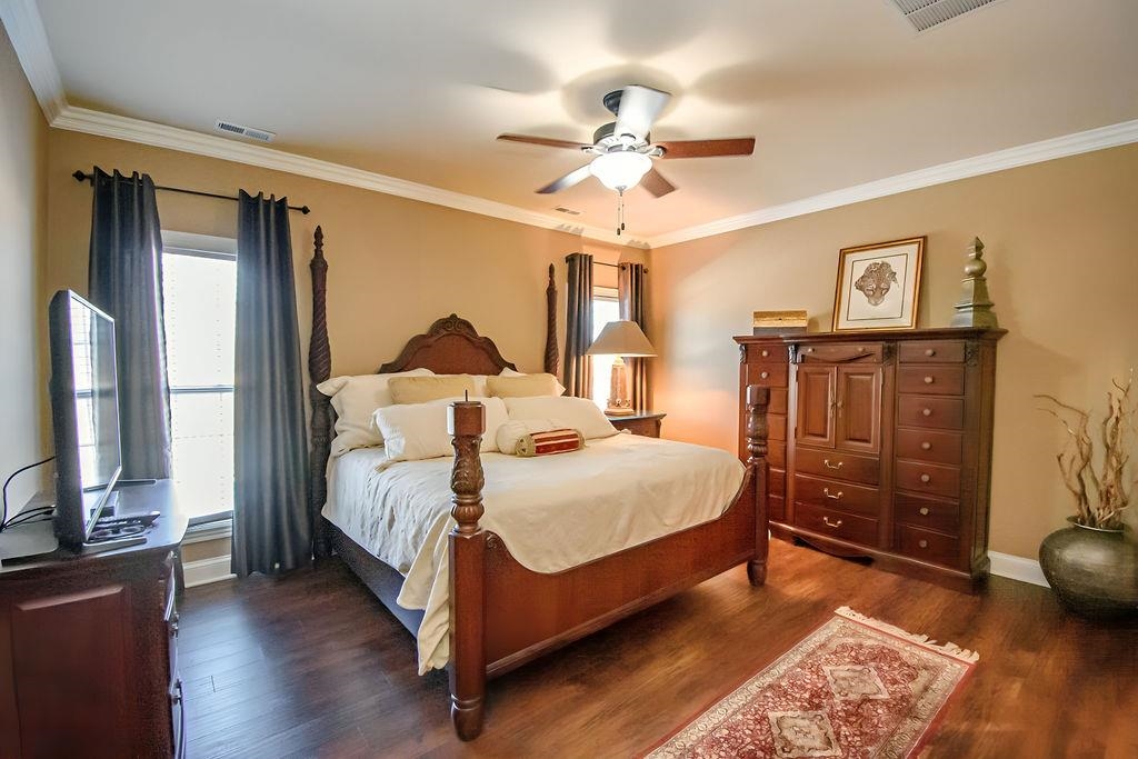 Spacious primary bedroom features hardwood flooring, crown moulding, ceiling fan and luxury bath.